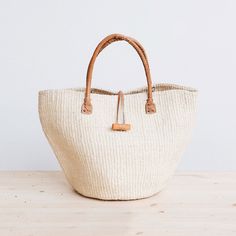 Rural Kamba women in Kenya hand-weave these beautiful handbags from tough sisal fibers. Sisal grows well in the semi-arid climate of eastern Kenya, and its spiky leaves contain long fibers that can be extracted for weaving.  approximate size: 10" diameter x 10" tall (without handle), 17" tall (with handle) leather hand Fair Trade Jute Crochet Bag For Daily Use, Woven Neutral Straw Bag, Neutral Woven Straw Bag, Artisan Crochet Bucket Bag In Natural Color, Eco-friendly Handwoven Natural Crochet Bag, Fair Trade Straw Bag For Travel, Fair Trade Crochet Bag For Daily Use, Artisan Jute Straw Bag, Fair Trade Beige Crochet Bag For Daily Use