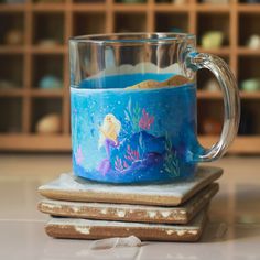 a glass mug with blue liquid in it sitting on top of coasters next to shelves