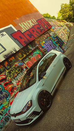 a white car parked in front of a wall covered with graffitti and graffiti