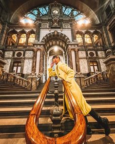 a man in a yellow coat leaning on a large wooden object at the bottom of some stairs