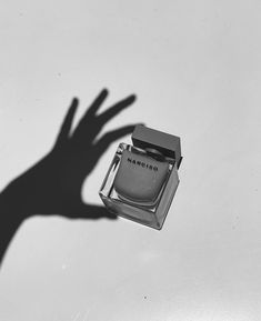 a person's hand casting a shadow over an empty perfume bottle