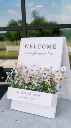 a welcome sign sitting on top of a table next to a flower pot filled with flowers