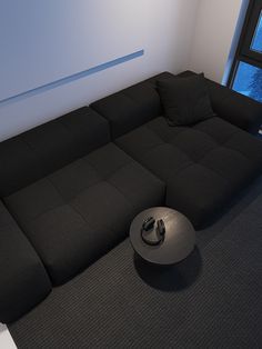 a black couch sitting in front of a window next to a round object on the floor