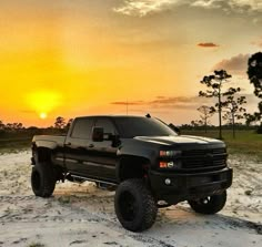 a black truck parked on top of a sandy beach next to the ocean at sunset