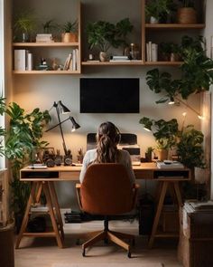 a woman sitting at a desk in front of a computer monitor with plants on it