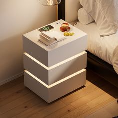 a night stand with two books on it next to a white bed and lamp in the corner