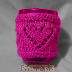 a pink knitted cup holder with holes in the middle and an image of a heart on it