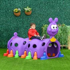 a little boy sitting on top of a purple toy train in front of a green wall