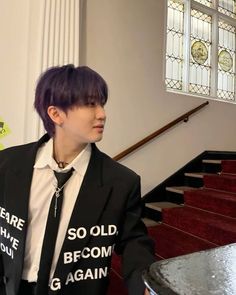 a man with purple hair wearing a black jacket and tie standing in front of some stairs