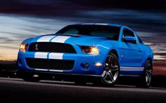 a blue mustang with white stripes parked in front of a sunset