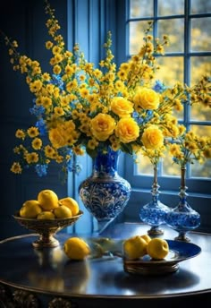 yellow flowers and lemons sit on a table in front of a blue glass window