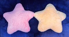 two star shaped stuffed animals sitting next to each other on a blue surface, one pink and one yellow