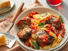 a white plate topped with meatballs covered in sauce and pasta next to bread on a table