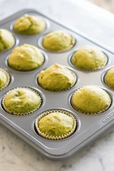 a muffin tin filled with green cupcakes on top of a marble counter