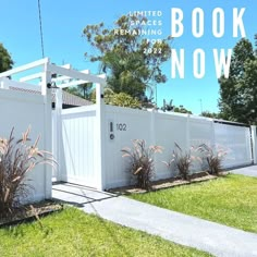 a white fence with the words book now on it in front of grass and trees