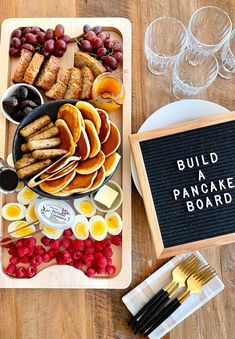 a wooden table topped with lots of different types of food next to wine glasses and utensils