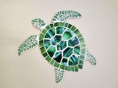 a sea turtle made out of green and white mosaic tiles on a wall in the shape of a shell