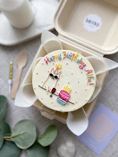 a decorated birthday cake in a box on a table next to flowers and utensils