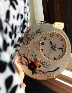 a woman holding up a clock with flowers on it