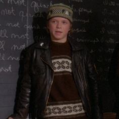 a woman standing in front of a blackboard with writing on it and wearing a hat