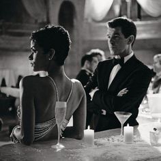 a man in a tuxedo standing next to a woman sitting at a bar