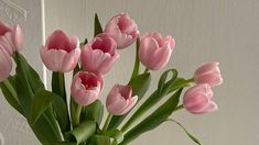 a vase filled with pink tulips sitting on top of a wooden table next to a white wall