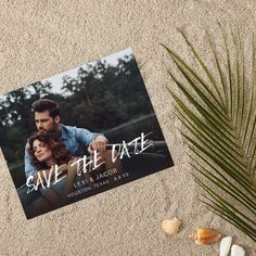 save the date photo card on sand with sea shells and palm tree in foreground