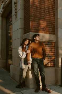 a man and woman standing next to each other in front of a tall brick building