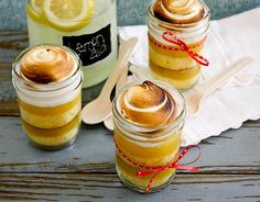 three jars filled with lemon custard and topped with marshmallows on a wooden table