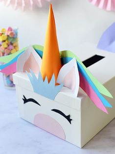 a paper unicorn head in a box with candy on the side and other decorations behind it