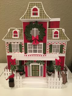 a red and white doll house with wreaths on the front door, windows, and shutters