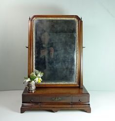 an old wooden mirror sitting on top of a table next to a vase with flowers