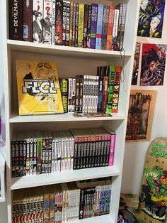 a bookshelf filled with lots of comics on top of white shelves next to a skateboard