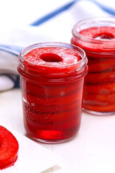 two jars filled with red jello sitting on top of a white table next to each other