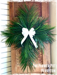 a wooden frame with a white bow and palm leaf wreath on the front of it