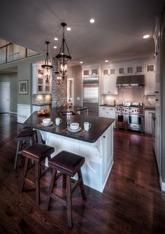 a large kitchen with an island and two stools next to it on a hard wood floor