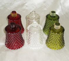 three different colored glass bottles sitting next to each other on a white cloth covered surface