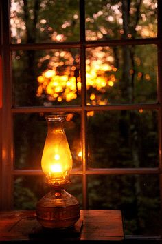 a lamp sitting on top of a wooden table next to a window with trees in the background