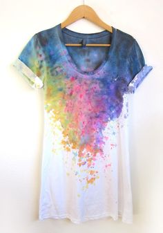 a t - shirt with colorful paint splattered on it hanging on a hanger