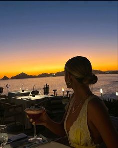 a woman sitting at a table with a drink in front of her and an ocean view