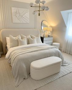 a bedroom with a large white bed and ottoman in the corner, along with two lamps on either side of the bed