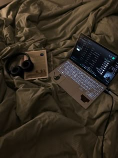 an open laptop computer sitting on top of a bed next to headphones and earbuds