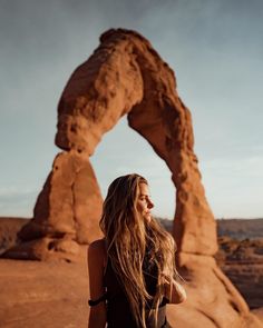 a woman standing in front of a rock formation with her hair blowing in the wind