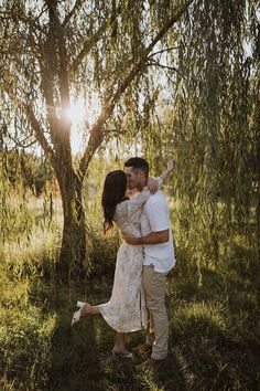 a man and woman kissing under a tree in the sun light at their engagement photo shoot