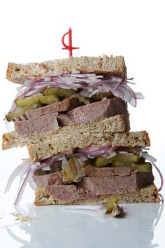 a sandwich with meat, onions and pickles is stacked on top of each other