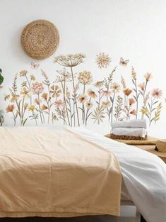 a bed sitting under a wall with flowers painted on it's side and a basket next to it