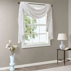 a living room with white walls and a window covered in sheer drapes on the windowsill