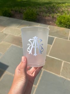 a hand holding up a clear glass with the letter s on it in front of a stone walkway