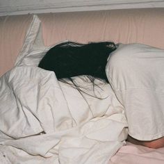 a person laying in bed with their head on the pillow and covering them from the wind