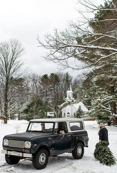 a black truck parked in the snow next to a christmas tree